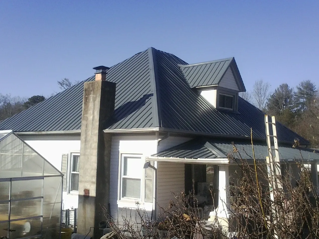 Dark blue standing seam metal roof on a white farmhouse with dormer — Slate & Tile Roof Repair by Roofing Brothers in Elkland