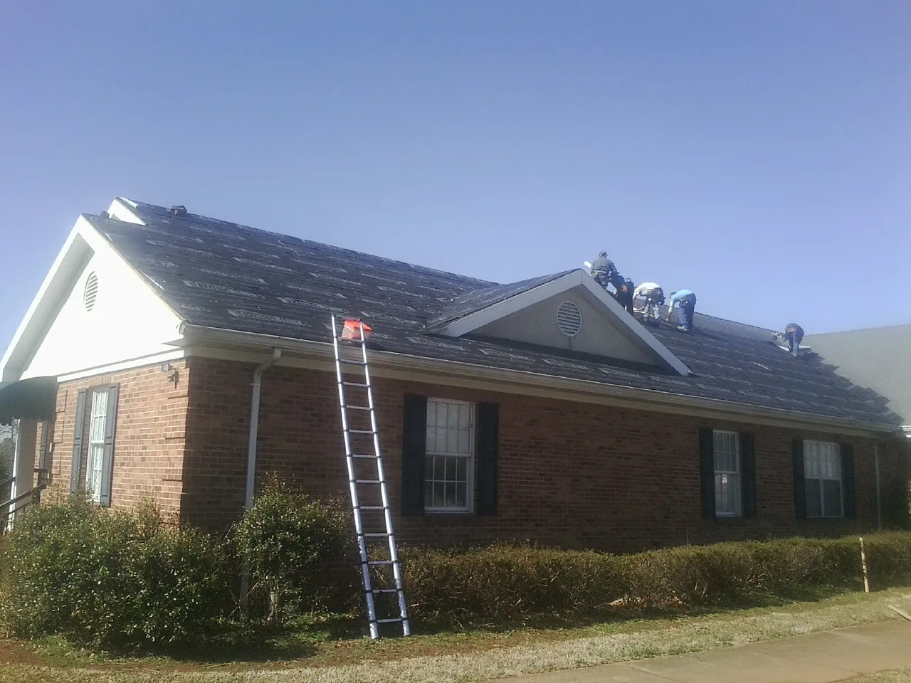 Crew tearing shingles off a brick ranch roof with a ladder set — Metal Roof Repair work by our crew in Elkland