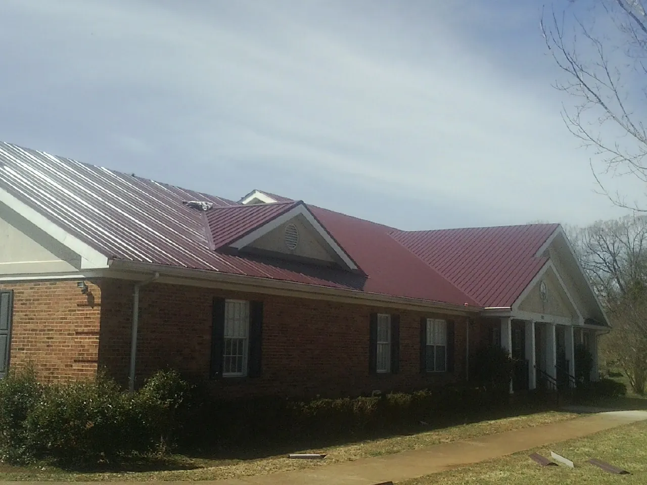 Red metal roof with gabled entries on a long brick building, from a Hail Damage Roof Repair job in Elkland