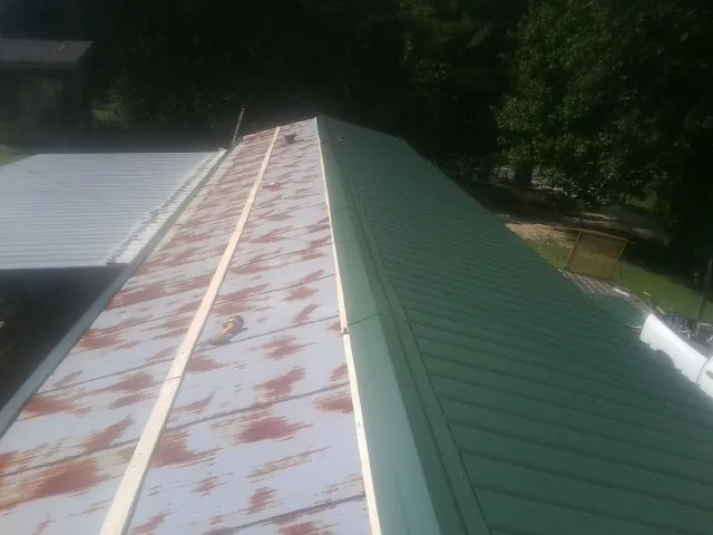 Old rusted panels beside newly installed green metal roofing — Wind Damage Roof Repair by Roofing Brothers in Elkland