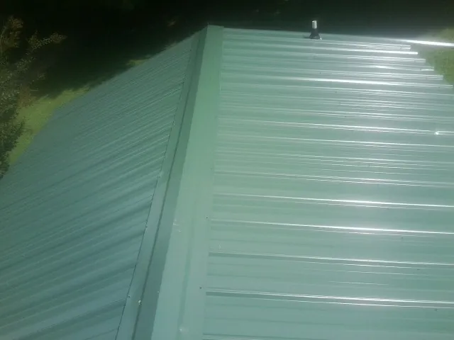 New green metal panels meeting at the ridge of a roof — Flat Roof Repair work by our crew in Elkland