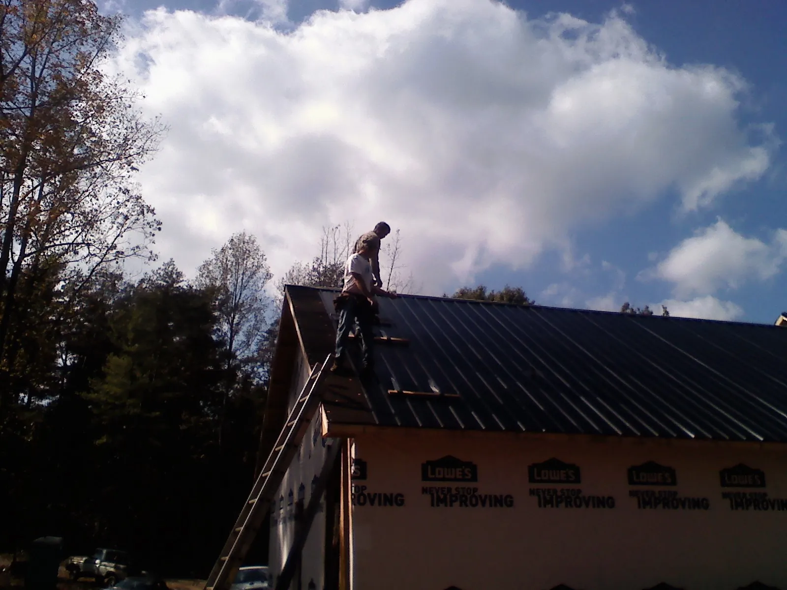 Roofer fastening dark metal panels high against a cloudy sky, from a Roof Inspection job in Elkland