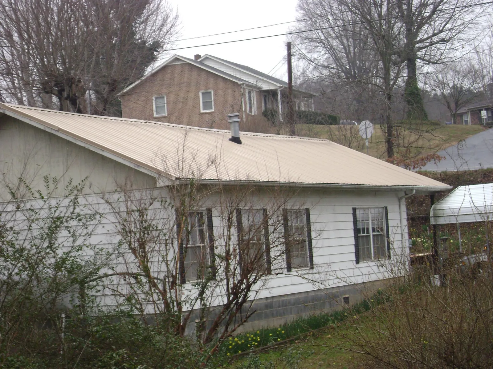 Tan metal roof on a white sided house set into a hillside — Commercial Roofing by Roofing Brothers in Elkland